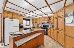 Kitchen featuring open shelves, black appliances, a center island, brown cabinets, and dark countertops - 
