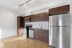 Kitchen with appliances with stainless steel finishes, modern cabinets, light wood-type flooring, dark brown cabinetry, and track lighting - 