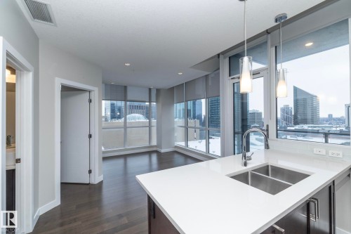 Kitchen featuring pendant lighting, dark wood finished floors, light stone countertops, open floor plan, and a city view - 1201 10238 103 Street, Edmonton, AB - Indoor Photo Showing Kitchen With Double Sink