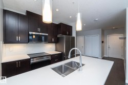 Kitchen featuring stainless steel appliances, pendant lighting, decorative backsplash, dark wood-type flooring, and a textured ceiling - 
