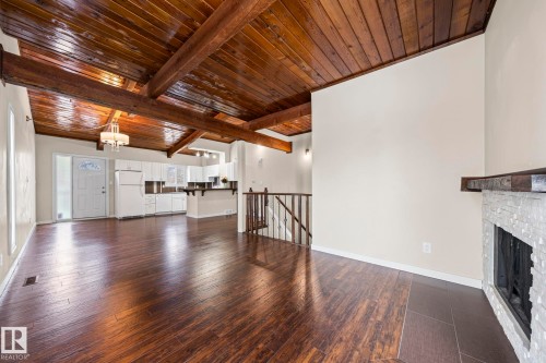 Unfurnished living room featuring dark wood-style floors, a stone fireplace, a wood ceiling with exposed beams, and a chandelier - 15 Northwoods Village, Edmonton, AB - Indoor Photo Showing Living Room With Fireplace