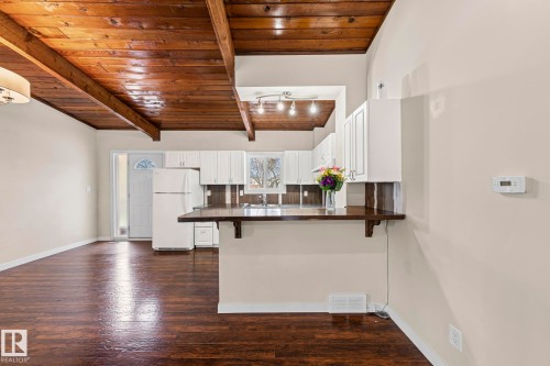 Kitchen with dark countertops, a wood ceiling with exposed beams, a breakfast bar, freestanding refrigerator, and dark wood finished floors - 15 Northwoods Village, Edmonton, AB - Indoor Photo Showing Kitchen