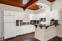 Kitchen featuring dark countertops, white appliances, wooden ceiling, white cabinetry, and a kitchen breakfast bar - 