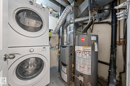 Laundry area with gas water heater, concrete floors, stacked washer and clothes dryer, and heating unit - 15 Northwoods Village, Edmonton, AB - Indoor Photo Showing Laundry Room
