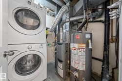 Laundry area with gas water heater, concrete floors, stacked washer and clothes dryer, and heating unit - 