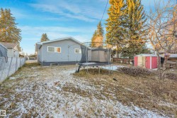 Snow covered back of property with a shed, a fenced backyard, a trampoline, and stucco siding - 