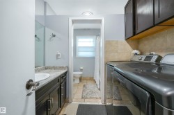 Full bath with vanity, a shower with shower curtain, washer and dryer, and light tile patterned floors - 