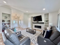 Living room featuring built in shelves, a tile fireplace, lofted ceiling, light wood-type flooring, and a chandelier - 