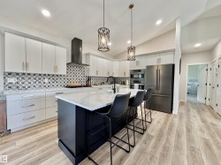 Kitchen featuring vaulted ceiling, decorative light fixtures, appliances with stainless steel finishes, tasteful backsplash, and an island with sink - 