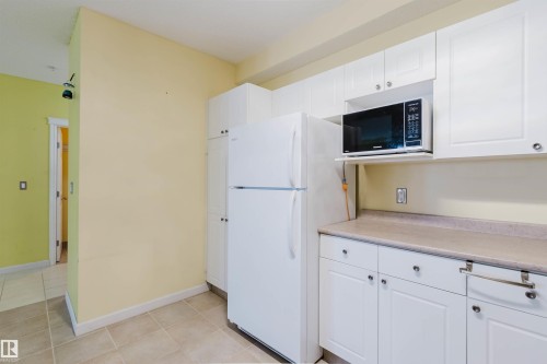 Kitchen with light countertops, white cabinets, light tile patterned flooring, and freestanding refrigerator - 406 9120 156 Street, Edmonton, AB - Indoor
