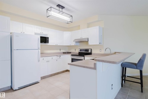 Kitchen with white appliances, a peninsula, a kitchen breakfast bar, and white cabinetry - 406 9120 156 Street, Edmonton, AB - Indoor Photo Showing Kitchen