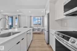 Kitchen with appliances with stainless steel finishes, white cabinetry, light stone countertops, recessed lighting, and light wood-type flooring - 
