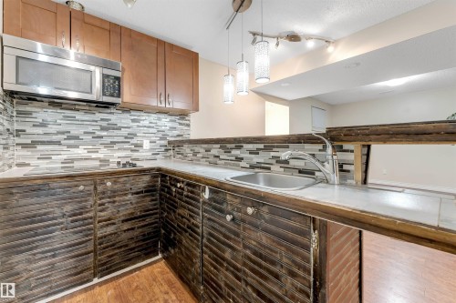 Kitchen featuring stainless steel microwave, pendant lighting, light wood-style floors, tasteful backsplash, and brown cabinetry - 18404 97A Avenue, Edmonton, AB - Indoor Photo Showing Kitchen With Upgraded Kitchen