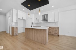 Kitchen with modern cabinets, white cabinetry, decorative light fixtures, a center island with sink, and wall chimney range hood - 