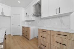 Kitchen with white cabinetry, island range hood, light stone counters, and light wood-style floors - 