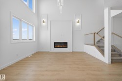 Unfurnished living room with a towering ceiling, light wood-type flooring, stairs, a glass covered fireplace, and plenty of natural light - 