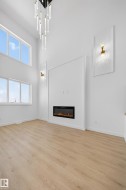 Unfurnished living room featuring a towering ceiling, light wood-style floors, and a glass covered fireplace - 