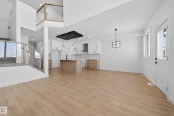 Unfurnished living room with healthy amount of natural light, light wood finished floors, stairs, recessed lighting, and a high ceiling - 