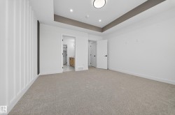 Unfurnished bedroom with a raised ceiling, connected bathroom, light carpet, and recessed lighting - 