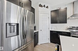Kitchen featuring appliances with stainless steel finishes, wall chimney exhaust hood, a textured ceiling, light stone counters, and light wood-style flooring - 