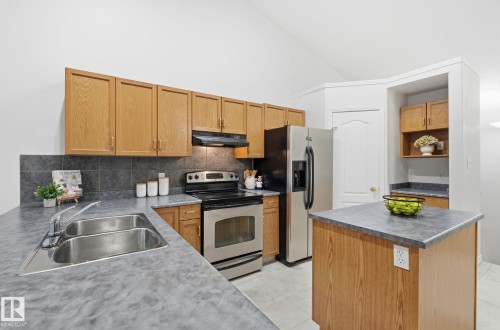 Kitchen with stainless steel appliances, a kitchen island, tasteful backsplash, high vaulted ceiling, and brown cabinets - 608 87 St, Edmonton, AB - Indoor Photo Showing Kitchen With Double Sink