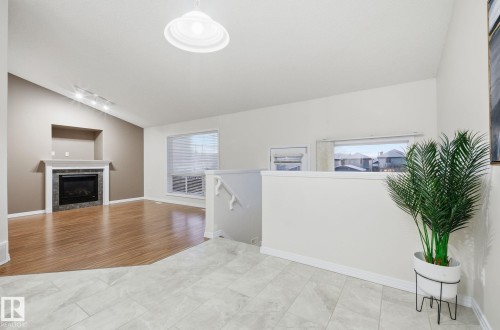 Living room with lofted ceiling, a tile fireplace, track lighting, healthy amount of natural light, and light wood-type flooring - 608 87 St, Edmonton, AB - Indoor With Fireplace