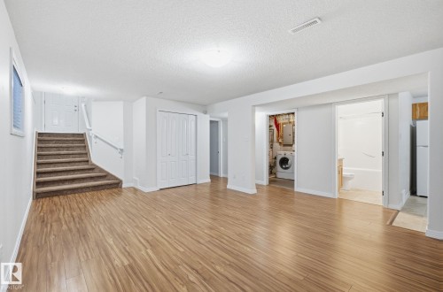 Finished below grade area with stairs, light wood-style flooring, a textured ceiling, washer / dryer, and freestanding refrigerator - 608 87 St, Edmonton, AB - Indoor Photo Showing Other Room