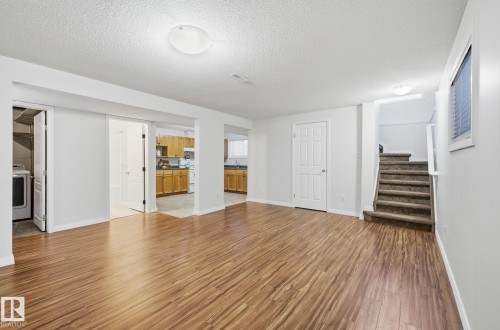 Unfurnished living room with a textured ceiling, light wood-style flooring, stairway, and washer / dryer - 608 87 St, Edmonton, AB - Indoor Photo Showing Other Room