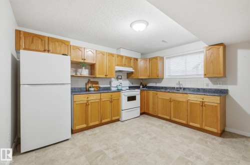 Kitchen with white appliances, dark countertops, decorative backsplash, open shelves, and a textured ceiling - 608 87 St, Edmonton, AB - Indoor Photo Showing Kitchen