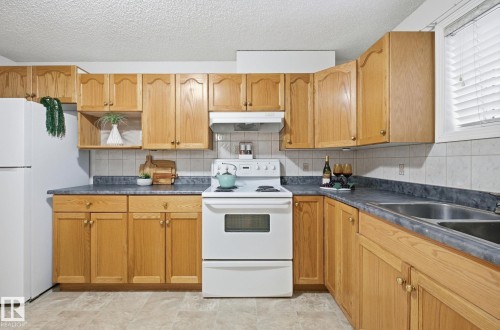 Kitchen with white appliances, dark countertops, under cabinet range hood, a textured ceiling, and backsplash - 608 87 St, Edmonton, AB - Indoor Photo Showing Kitchen