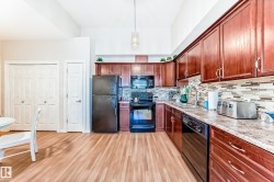 Kitchen featuring black appliances, light countertops, light wood-style floors, hanging light fixtures, and backsplash - 