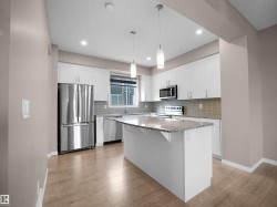 Kitchen featuring stainless steel appliances, pendant lighting, light stone counters, and decorative backsplash - 