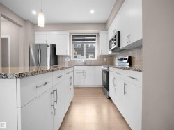 Kitchen featuring appliances with stainless steel finishes, dark stone countertops, hanging light fixtures, white cabinetry, and decorative backsplash - 