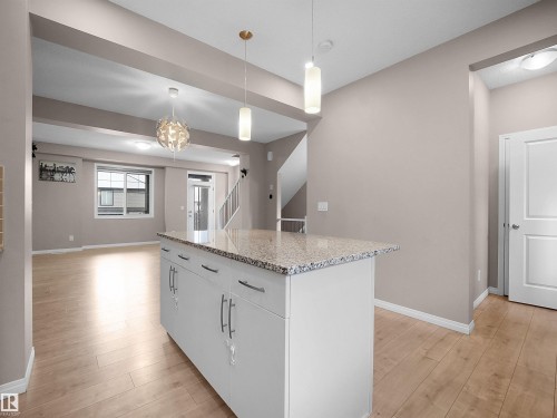 Kitchen featuring pendant lighting, light stone counters, white cabinetry, a kitchen island, and light wood-style floors - 2080 Wonnacott Way, Edmonton, AB - Indoor Photo Showing Kitchen