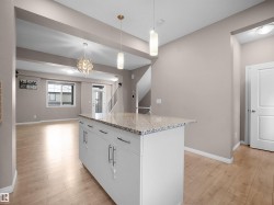 Kitchen featuring pendant lighting, light stone counters, white cabinetry, a kitchen island, and light wood-style floors - 