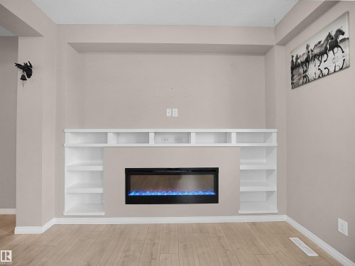 Detailed view of built in features, a glass covered fireplace, and wood finished floors - 2080 Wonnacott Way, Edmonton, AB - Indoor With Fireplace