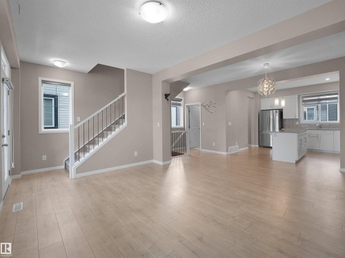 Unfurnished living room featuring stairs, light wood-style flooring, a textured ceiling, and a chandelier - 2080 Wonnacott Way, Edmonton, AB - Indoor