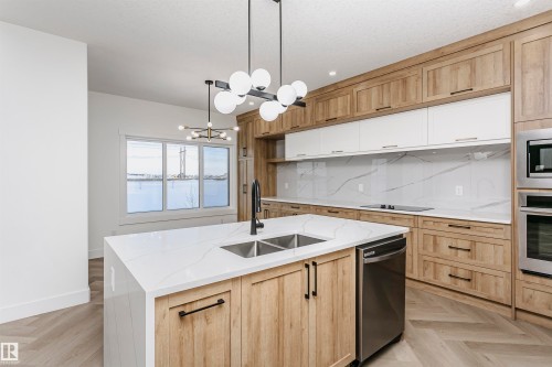 Kitchen featuring pendant lighting, light stone counters, light brown cabinets, stainless steel appliances, and a chandelier - 220 Edgemont Green Green, Edmonton, AB - Indoor Photo Showing Kitchen With Double Sink With Upgraded Kitchen