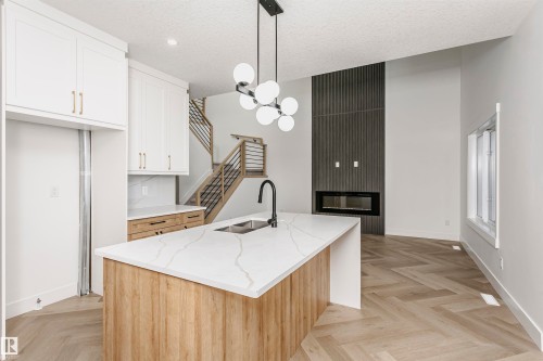 Kitchen featuring white cabinets, a large fireplace, hanging light fixtures, light stone countertops, and a chandelier - 220 Edgemont Green Green, Edmonton, AB - Indoor Photo Showing Kitchen