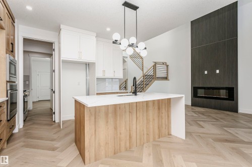 Kitchen with a chandelier, light stone countertops, hanging light fixtures, a kitchen island with sink, and a glass covered fireplace - 220 Edgemont Green Green, Edmonton, AB - Indoor Photo Showing Kitchen