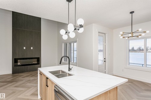 Kitchen featuring a chandelier, light brown cabinetry, an island with sink, light stone countertops, and a textured ceiling - 220 Edgemont Green Green, Edmonton, AB - Indoor Photo Showing Kitchen With Double Sink