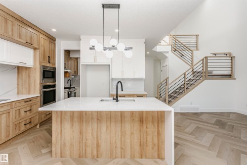 Kitchen featuring light stone countertops, a center island with sink, decorative light fixtures, stainless steel appliances, and backsplash - 220 Edgemont Green Green, Edmonton, AB - Indoor Photo Showing Kitchen With Upgraded Kitchen