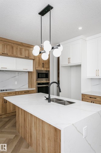 Kitchen with light stone counters, hanging light fixtures, appliances with stainless steel finishes, a textured ceiling, and a kitchen island with sink - 220 Edgemont Green Green, Edmonton, AB - Indoor Photo Showing Kitchen With Double Sink With Upgraded Kitchen