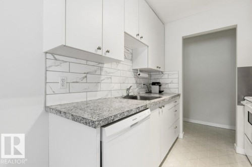 Kitchen with white appliances, white cabinets, tasteful backsplash, light countertops, and light floors - 124 5730 Riverbend Road, Edmonton, AB - Indoor Photo Showing Kitchen