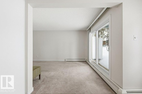 Unfurnished room with baseboard heating, light carpet, and a textured ceiling - 124 5730 Riverbend Road, Edmonton, AB - Indoor Photo Showing Other Room