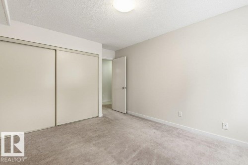 Unfurnished bedroom with a textured ceiling, light carpet, and a closet - 124 5730 Riverbend Road, Edmonton, AB - Indoor Photo Showing Other Room
