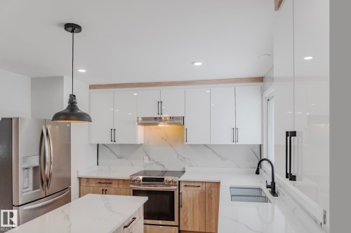 Kitchen featuring appliances with stainless steel finishes, light stone countertops, modern cabinets, pendant lighting, and recessed lighting - 13711 133 Avenue, Edmonton, AB - Indoor Photo Showing Kitchen