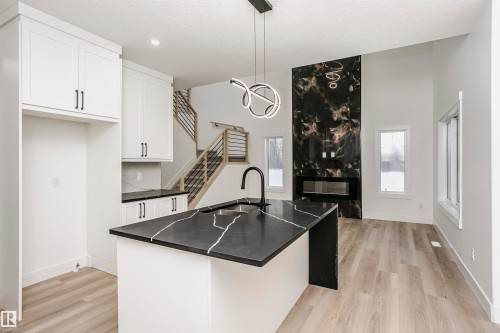 Kitchen with white cabinetry, hanging light fixtures, light wood-type flooring, an island with sink, and a textured ceiling - 804 Elderberry Crest, Edmonton, AB - Indoor Photo Showing Kitchen