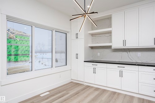 Kitchen featuring open shelves, tasteful backsplash, white cabinets, light wood finished floors, and a chandelier - 804 Elderberry Crest, Edmonton, AB - Indoor