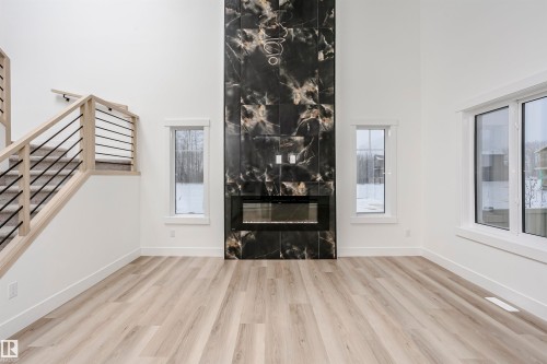 Unfurnished living room featuring a towering ceiling, healthy amount of natural light, wood finished floors, stairs, and a fireplace - 804 Elderberry Crest, Edmonton, AB - Indoor With Fireplace